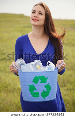 Young woman holding a blue recycling bin with plastic bottles