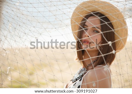 Young fashion model in straw hat  behind the fishing net outdoors near river. Professional styling,hairs, make-up