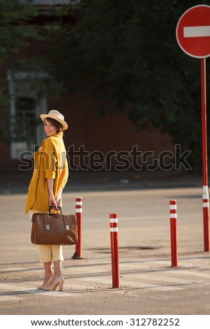 Young happy funny dressed woman with retro suitcase stands on the street near red road sign