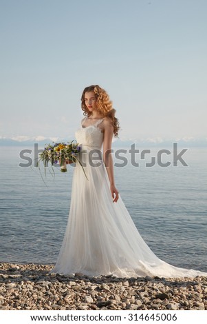 Young bride with flowers stands near water with colorful posy. Professional style and make-up