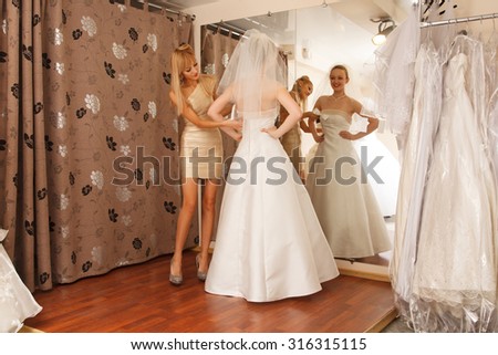 A Bride-To-Be Trying On A Wedding Dress with a girlfriend   in a Bridal Boutique.