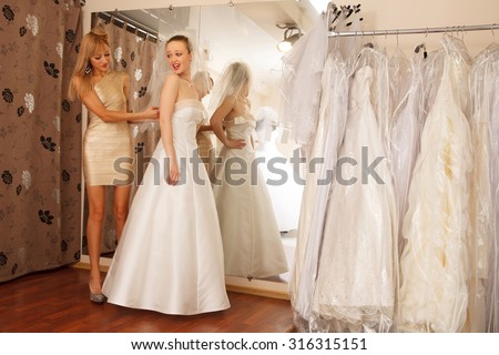 Two girlfriends - A Bride-To-Be and bridesmaid Trying On A Wedding dress