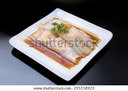 Chinese rice noodle roll with shrimp topping with parsley on white plate over black table at Hong Kong dim sum restaurant