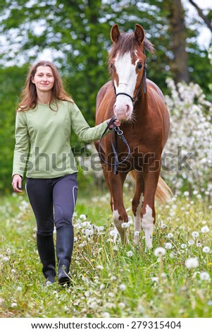 Beautiful smiling young woman leading a horse.
