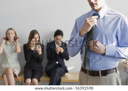 Man adjusting his tie, preparing for job interview, with fellow applicants in background