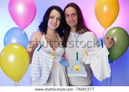 Happy pregnant couple holding baby\'s clothe