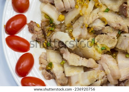 A White Plate Full of Oily Pork Meat With The Border Decorated With Cherry Tomatoes.