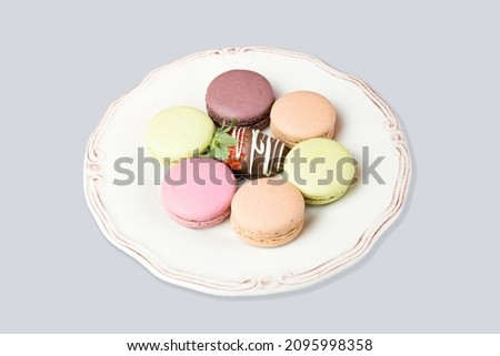 Six tasty and colorful macarons and a chocolate strawberry on an elegance vintage plate isolated on white. French macarons on stylish plate. Close up six meringue and a chocolate strawberry. Beze. Imagine de stoc © 