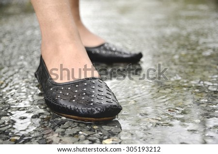 Girl in fashion shoes is standing in the puddle in the middle of the rain