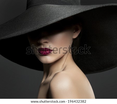 beautiful woman in a black broad-brim  hat with red lips and a mole on her cheek