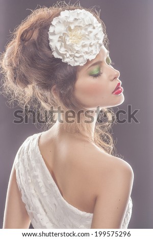 beautiful young woman with fashion make-up, volume hairdo and big flower in her hair. Fashion bride. Trendy wedding look. Makeup with Bright eyes and lips