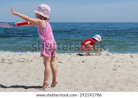 Funny little girls (sisters) play badminton on the beach.