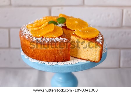 Sliced fluffy chiffon cake with orange slices on cake plate. Light background, selective focus.