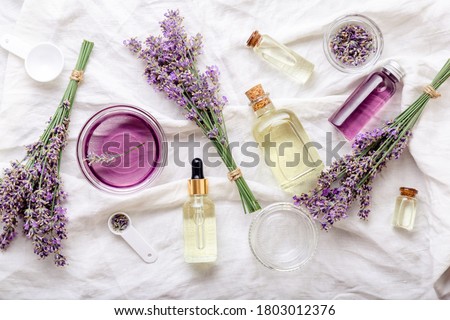 Lavender oils serum and lavender flowers on white fabric. Skincare cosmetics products. Set natural spa beauty products. Lavender essential oil, serum, body butter, massage oil, liquid. Flat lay