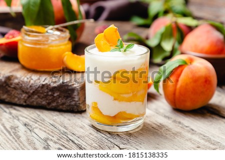 Peach fruit dessert in glass cup on rustic wooden table with fresh peach fruit, peach jam. Homemade dessert with fruits. Fruit salad with yogurt or sour cream.
