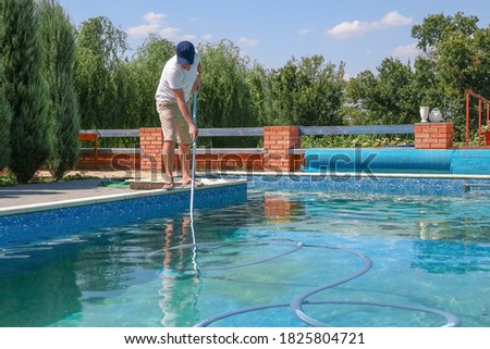 Cleaner swimming pool. Man cleaning outdoor swimming pool with vacuum tube cleaner in summer. Seasonal preparations. Cleaning systems for swimming pools. Dirty outdoor pool