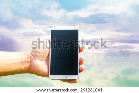 Man hand holding smartphone on sky pastel tone background soft focus.