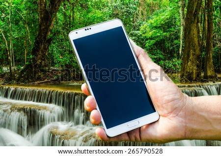 Man hand holding smartphone on the forest waterfall backgrounds soft focus.