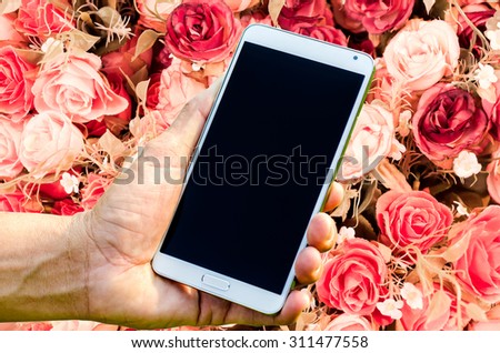 Man hand holding smartphone on rose vintage background soft focus.