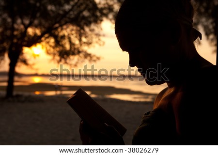 Silhouette of a woman sitting on the beach and reading a book