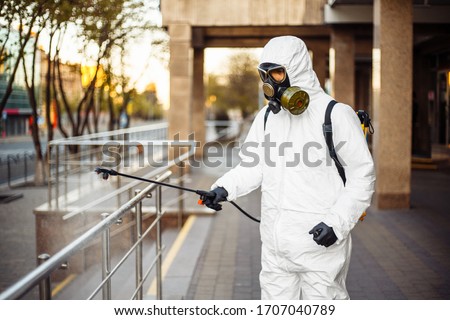 Man sprays disinfector onto the railing wearing coronavirus protective suit and equipment. Cleaning and sterilizing the not crowded city streets. Covid-19 nCov2019 spread prevention Zdjęcia stock © 