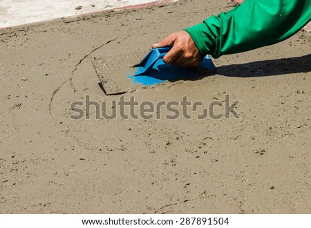 Close-up of hand using trowel to finish wet concrete floor