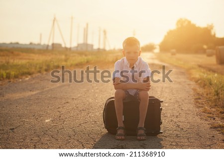 the child sits on a suitcase in the summer sunny day, the traveler