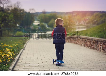 Little cute boy riding and his scooter bicycle in summer, outdoors, rear view
