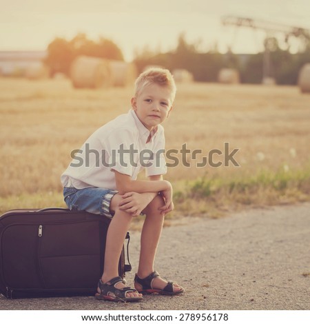 the child sits on a suitcase in the summer sunny day, the traveler. Toned image