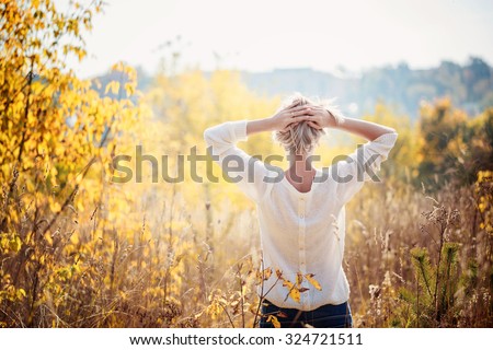 Happy young girl enjoying the beauty of sunny autumn day  in high grass in an autumn park. View from a back.