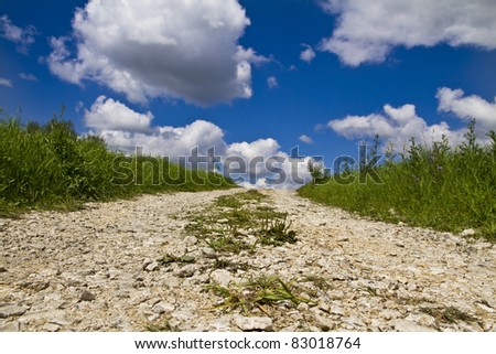 Countryside stone road in fields and blue sky with clouds