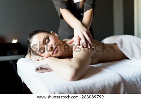 Beautiful, young and healthy woman having her shoulder and body massaged by a professional masseur at a spa center