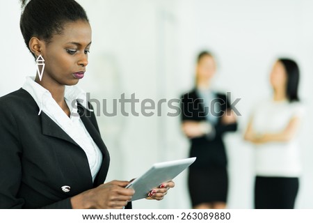 Businesswoman holding a tablet and concentrating on the contents with two colleagues blurred out in the background