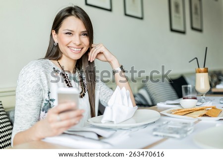 Beautiful smiling lady sitting in a restaurant at a table and holding her cell phone