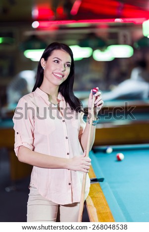 Young beautiful woman chalking the snooker cue and smiling in a club