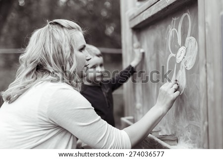 Beautiful mother and son drawing on blackboard with chalk