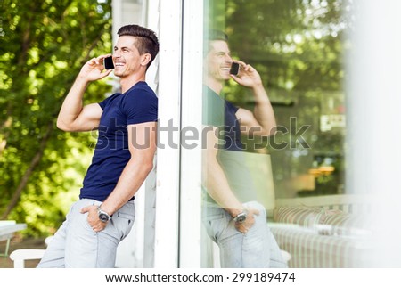 Handsome man talking on the phone outdoors and his reflection is present