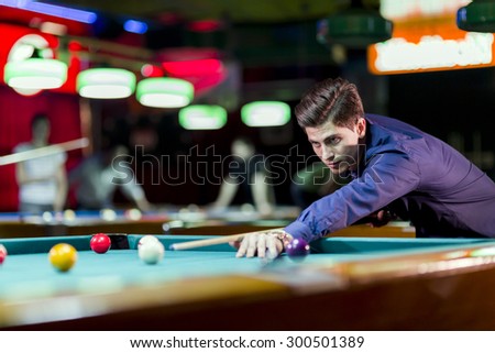 Young handsome man leaning over the table while playing snooker