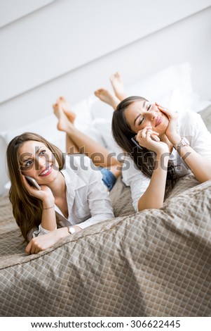 Two beautiful girls talking on the phone and smiling while lying on a luxurious  bed