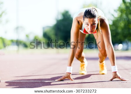 Beautiful female sprinter getting ready for the run during summer