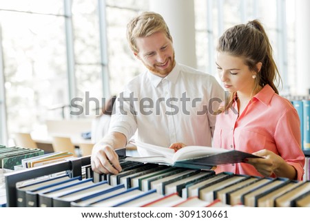 Two  smart students reading and studying in library whole searching through books on the shelves