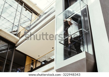 Businessman taking modern glass elevator to the upper floors