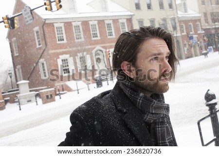 Side profile of an attractive young man looking up during a snow storm while wrapped in black winter clothes.