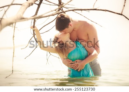 handsome man kiss his beautiful blonde woman in blue dress stand in sea water