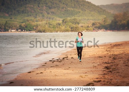 brunette girl in sports clothes runs from distance on sand beach at low tide against sea at dawn