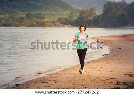 brunette girl in sports clothes runs on sand beach at low tide against sea at dawn
