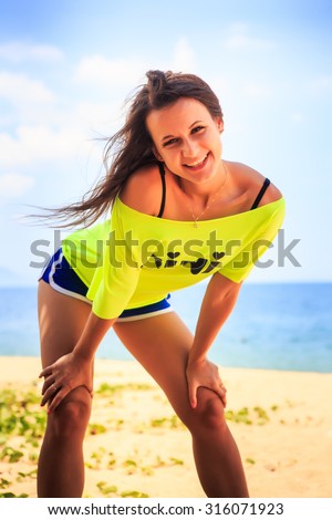european slim girl closeup in lemon yellow t-shirt bows down laughs and shows tongue on sand beach against sea