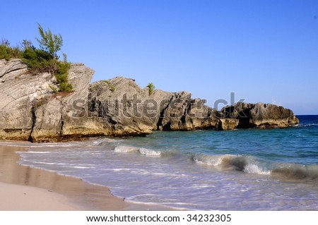 Bermuda beach during a hot summer day.  Photo includes the sky, rocky coastline, pink sand and the tide rolling in.