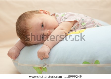 One month old baby lying on his tummy on the blue pillow. Baby looking at the camera. Selective focus on baby face