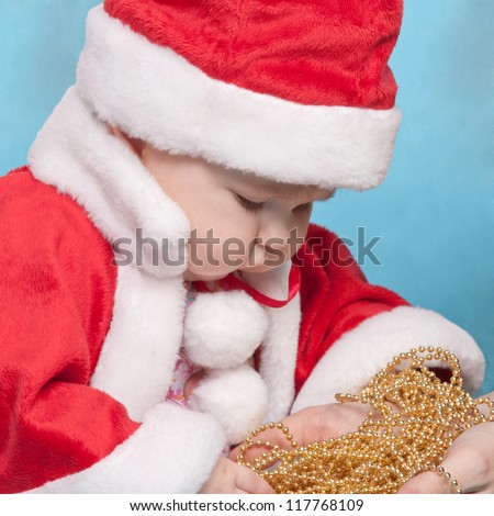Six month old Santa Claus baby dressed in red looking at golden beads